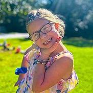 Ella is registered to the contest to win money with this photo: child, girl, glasses, floral_dress, outdoor, sunlight, green_grass, smiling, playful_pose, bracelet, nature, daylight, happy, portrait, summer, trees, sunshine, casual, fashion, young