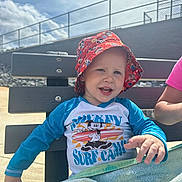 Eli joined the competition — help win amazing prizes! toddler, child, bench, hat, bucket_hat, mickey_mouse, surf_camp, towel, outdoor, sunny, sky, fence, smiling, happy, person, clothing, daylight, portrait, casual, playful