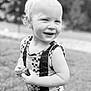 Eli is registered to the contest to win money with this photo: toddler, child, smiling, outdoor, grass, keychain, beads, tassel, sleeveless, patterned_clothing, blond_hair, portrait, happy, cute, young_child, standing, nature, black_and_white, person, close_up