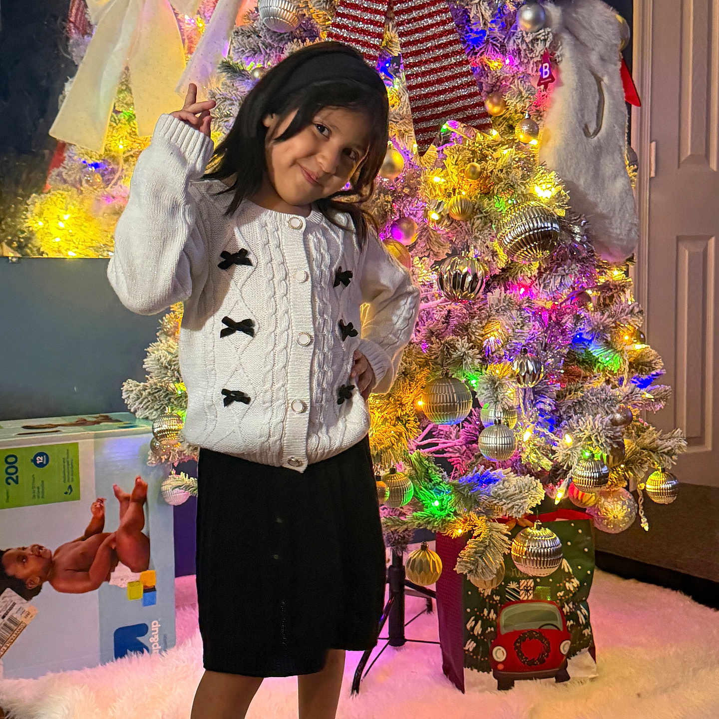 Verónica is registered to the contest to win money with this photo: child, girl, smiling, portrait, christmas, christmas_tree, festive, holiday, ornaments, fairy_lights, santa_hat, winter, sweater, skirt, standing, indoor, home, gifts, colorful, decoration