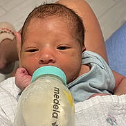 Liam joined the competition — help win amazing prizes! baby, newborn, infant, feeding, bottle, milk, blanket, car_print, person, skin, hand, foot, floor, tile, clothing, sleepy, resting, indoors, closeup, portrait