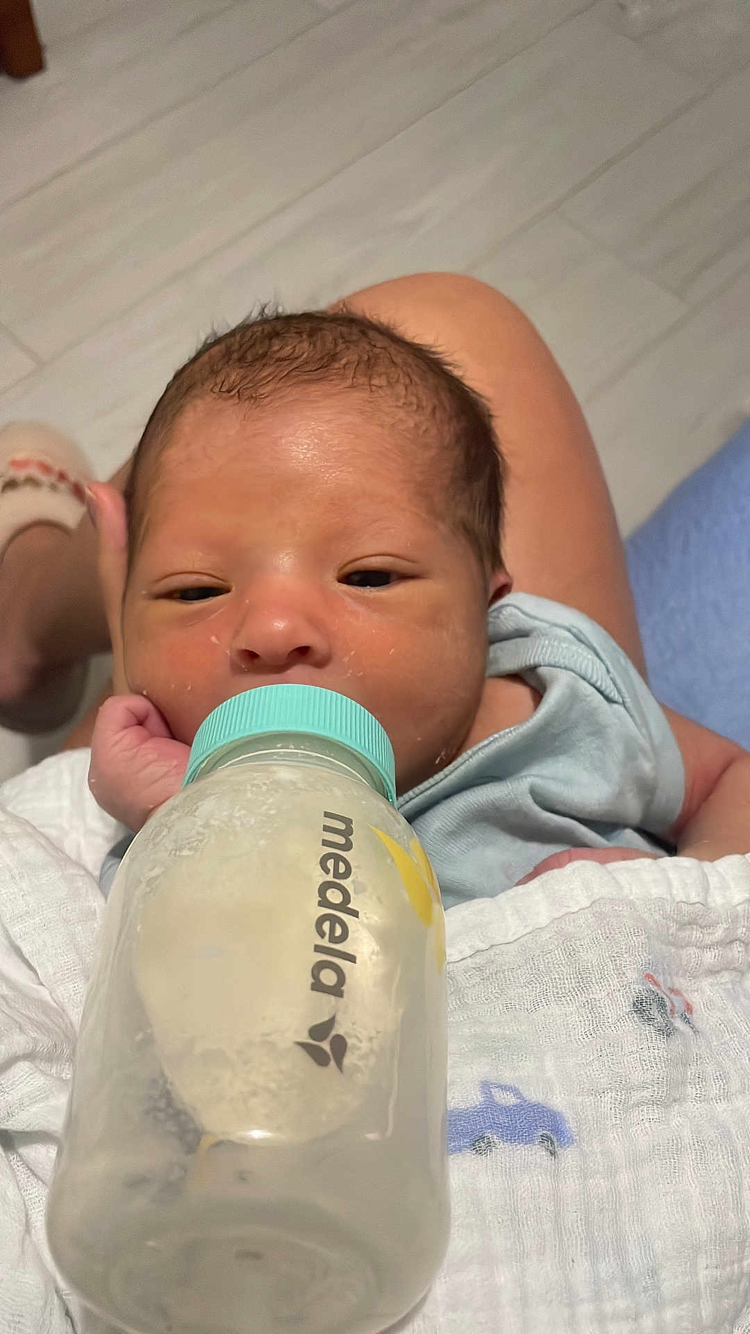 Liam joined the competition — help win amazing prizes! baby, newborn, infant, feeding, bottle, milk, blanket, car_print, person, skin, hand, foot, floor, tile, clothing, sleepy, resting, indoors, closeup, portrait