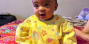 Nova joined the competition — help win amazing prizes! baby, child, yellow_outfit, bows, hair_bows, rainbow_pattern, strawberry_pattern, bedspread, colorful, indoor, sitting, curious, person, foot, hand, head, face, expression, wall_decoration, cozy