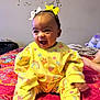 baby, child, smiling, yellow_clothing, bows, bed, colorful, happy, indoor, cute, infant, person, foot, patterned_bedspread, rainbow, strawberry, playful, joyful, headband, toddler