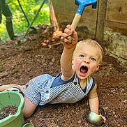 Marcel a rejoint le concours — aidez-le/la à gagner de superbes lots ! toddler, child, blue_eyes, striped_overalls, shovel, metal_bowl, green_bucket, green_scoop, dirt, soil, outdoor, playing, garden, wooden_wall, nature, sunlight, happy, expression, summer, casual_clothing