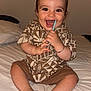 baby, child, smiling, happy, sitting, bed, clothing, shorts, shirt, patterned, indoors, chewing, straw, bracelet, feet, toes, portrait, cute, person, home