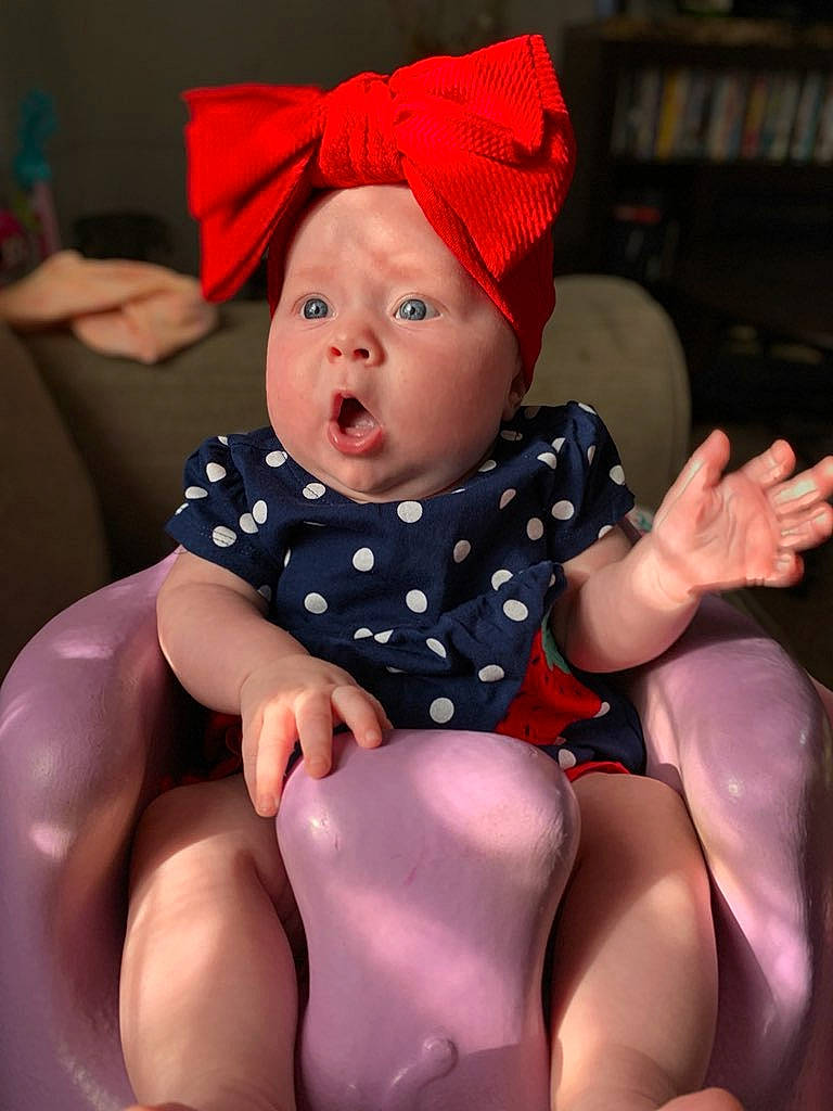 Alyvia joined the competition — help win amazing prizes! baby, baby_toddler_clothing, bookcase, comfort, finger, foot, hat, headwear, human_body, human_leg, knee, lap, mouth, muscle, person, pink, shelf, sleeve, sportswear, surprise