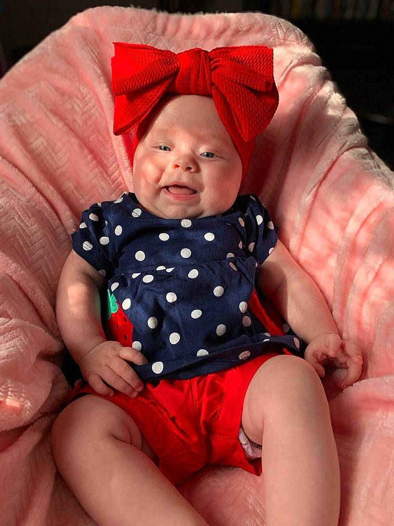 Alyvia is registered to the contest to win money with this photo: arm, baby, baby_toddler_clothing, comfort, face, finger, hand, head, headgear, headwear, human_body, lap, leg, organ, person, photograph, pink, skin, sleeve, smile