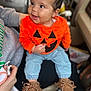 Alyza is registered to the contest to win money with this photo: baby, child, infant, orange_sweater, pumpkin_face, blue_jeans, moccasins, person, smile, happy, indoor, seated, cute, face, hands, clothing, footwear, lap, joy, casual