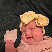 Emilia is registered to the contest to win money with this photo: baby, infant, sleeping, headband, bow, mitten, pink_clothing, couch, soft_fabric, cute, child, chubby_cheeks, portrait, indoor, relaxed, peaceful, closeup, skin, hand, cozy