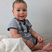 Noah is registered to the contest to win money with this photo: baby, child, infant, smiling, sitting, portrait, indoors, bed, blanket, striped_clothing, short_sleeves, bare_feet, bedroom, wall, cozy, happy, face, person, photography, natural_light