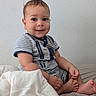 baby, child, infant, smiling, sitting, portrait, indoors, bed, blanket, striped_clothing, short_sleeves, bare_feet, bedroom, wall, cozy, happy, face, person, photography, natural_light