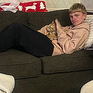 Thor is registered to the contest to win money with this photo: person, cat, couch, blanket, indoor, relaxed, young_person, orange_cat, furniture, home, cozy, patterned_wall, sitting, casual_clothing, hoodie, black_pants, tabby_cat, carpet, table, living_room