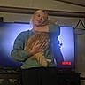 Thor is registered to the contest to win money with this photo: person, cat, indoor, television, netflix, sweatshirt, orange_cat, hugging, blonde_hair, wall_sign, furniture, cabinet, cozy, casual_clothing, living_room, pet, screen, silhouette, relaxed, home