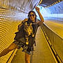 woman, cat, backpack, tunnel, sunglasses, brick_wall, street, sidewalk, railings, lighting, smile, playful_pose, shorts, urban, animal, pet, walking, road, daylight, fun