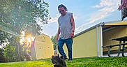 Teddy joined the competition — help win amazing prizes! bench, building, casual_clothing, clouds, daytime, dog, grass, greenery, man, nature, outdoor, pet, playful, running, shed, sky, sunflare, sunlight, tree, yard