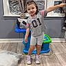 Emerson joined the competition — help win amazing prizes! child, indoor, curtains, window, toy_table, floor, pillow, sneakers, grey_clothing, smile, standing, arm_outstretched, wooden_floor, playful, young_child, shorts, tshirt, home, curtain_tie, person