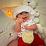 baby, smiling, white_hat, red_shorts, plush_toy, teddy_bear, milestone_sign, 2_months, heart_pattern, cute, infant, indoor, soft_lighting, cushion, happy, child, portrait, sitting, cozy, celebration