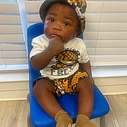 Kaison is registered to the contest to win money with this photo: baby, child, indoor, blue_chair, hat, shorts, socks, tshirt, face, hand, floor, window, blinds, curious, seated, portrait, person, cute, expression, furniture
