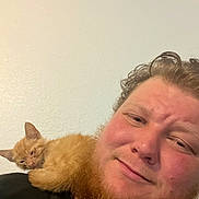 Dash is registered to the contest to win money with this photo: cat, kitten, orange_cat, pet, man, person, beard, selfie, portrait, close_up, indoors, wall, shoulder, cuddling, sleepy, relaxed, furry, ginger, human_animal_bond, black_shirt