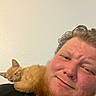 cat, kitten, orange_cat, pet, man, person, beard, selfie, portrait, close_up, indoors, wall, shoulder, cuddling, sleepy, relaxed, furry, ginger, human_animal_bond, black_shirt