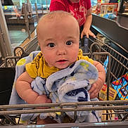 Milo joined the competition — help win amazing prizes! baby, child, shopping_cart, blanket, person, woman, grocery_store, indoor, shopping, clothing, face, curious, retail, cart, infant, casual, young_child, parent, supermarket, focus