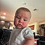 baby, child, indoor, living_room, couch, striped_clothing, face, hand, person, furniture, home, kitchen, cabinet, red_cheeks, holding, young_child, casual, portrait, expression, human