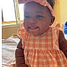 Nova is registered to the contest to win money with this photo: baby, child, girl, smiling, pink_bow, checkered_dress, indoor, bed, window, sunlight, cute, happy, portrait, sitting, infant, clothing, headwear, playful, skin, person
