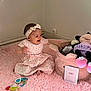 baby, child, pink_dress, headband, plush_toy, stuffed_animal, pink_rug, toy_basket, indoor, corner, wall_socket, happy, smiling, sitting, playing, floor, soft_texture, baby_toys, person, infant