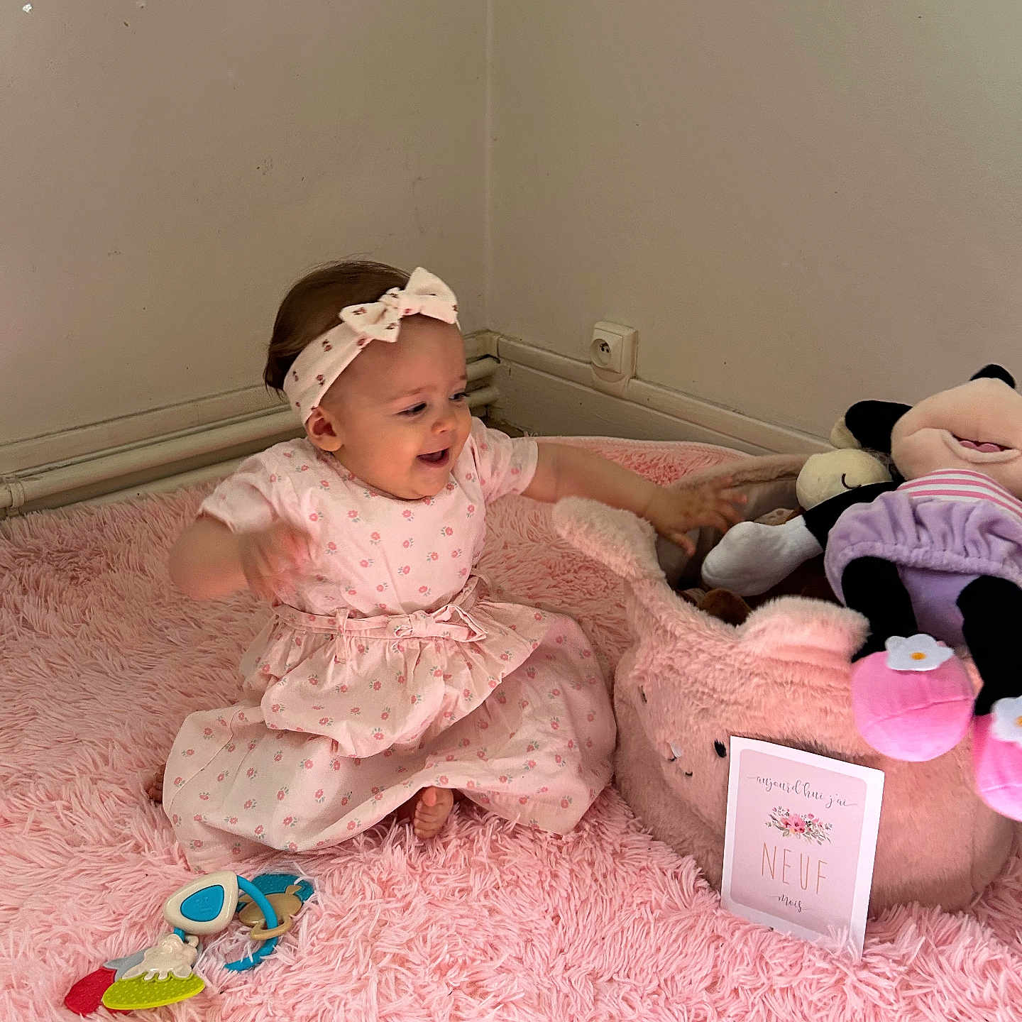 Ambre a rejoint le concours — aidez-le/la à gagner de superbes lots ! baby, baby_toys, child, corner, floor, happy, headband, indoor, infant, person, pink_dress, pink_rug, playing, plush_toy, sitting, smiling, soft_texture, stuffed_animal, toy_basket, wall_socket