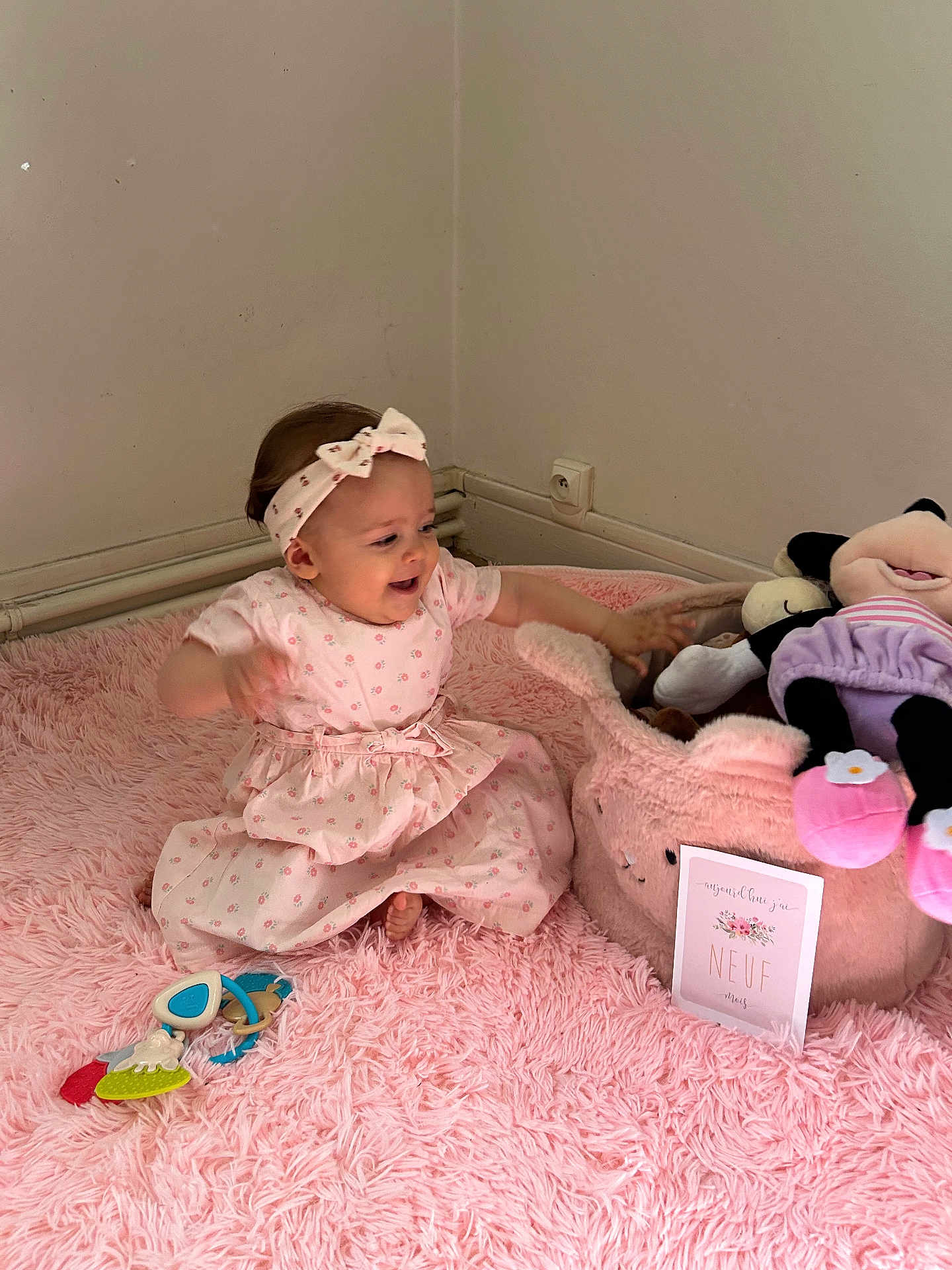 Ambre a rejoint le concours — aidez-le/la à gagner de superbes lots ! baby, child, pink_dress, headband, plush_toy, stuffed_animal, pink_rug, toy_basket, indoor, corner, wall_socket, happy, smiling, sitting, playing, floor, soft_texture, baby_toys, person, infant