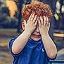 Kaïs participe au concours pour gagner de l'argent avec cette photo : child, curly_hair, blue_shirt, covering_face, playful, outdoor, park, daylight, person, smile, hands, young, red_hair, casual_clothing, nature, trees, background_blur, cute, fun, portrait