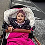 baby, stroller, blanket, jacket, headwear, sidewalk, street, car, pedestrian_crossing, child, urban, winter_clothing, happy, portrait, outdoor, road, person, baby_smile, warm_clothing, cozy