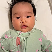 Justine is registered to the contest to win money with this photo: baby, infant, face, hair, onesie, flamingo_pattern, mint_green, pink, sleepwear, cute, child, portrait, lying_down, skin, expression, small_hand, indoor, soft_lighting, closeup, young