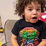 child, toddler, curly_hair, marvel_comics, tshirt, couch, indoor, expression, open_mouth, person, sitting, casual_clothing, young_child, facial_expression, home, reaction_emoji, cute, curly_hair_child, black_tshirt, marvel_characters