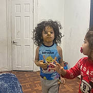 Jayden joined the competition — help win amazing prizes! child, kid, curly_hair, baby_shark, tank_top, food_on_face, food_on_hands, pacifier, red_sweater, wooden_floor, white_door, indoor, two_children, playful, candid, messy, person, young, home, interaction