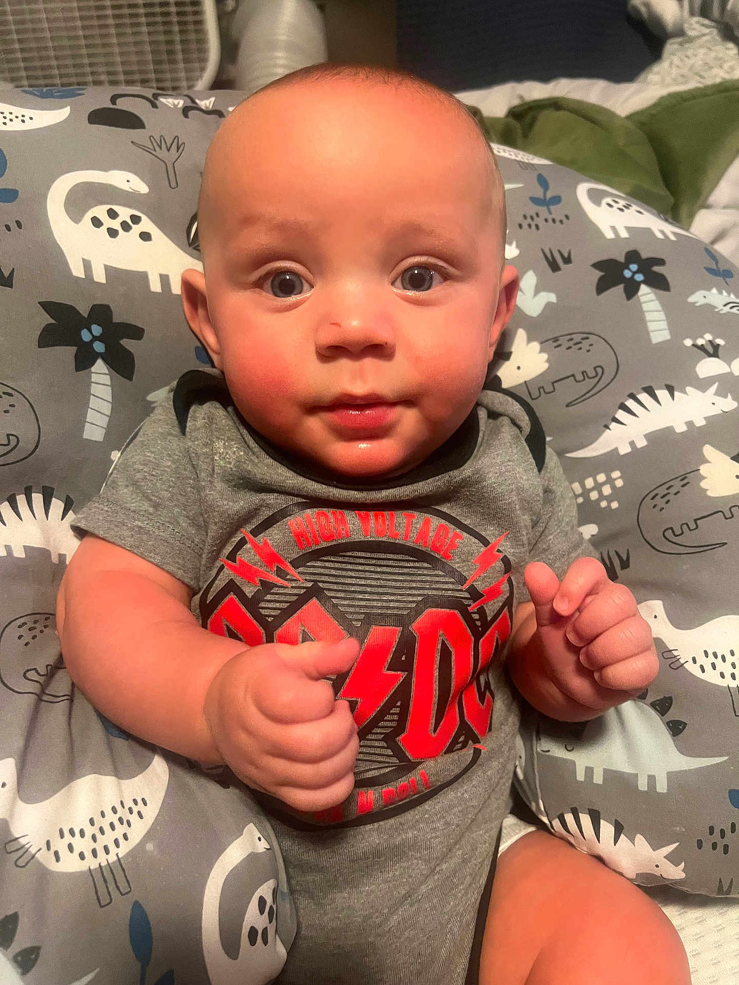 Mythiyus is registered to the contest to win money with this photo: baby, infant, child, onesie, gray_clothing, acdc, dinosaur_pattern, cushion, indoor, cute, chubby_cheeks, sitting, portrait, expression, furniture, hand, face, head, eyes, skin