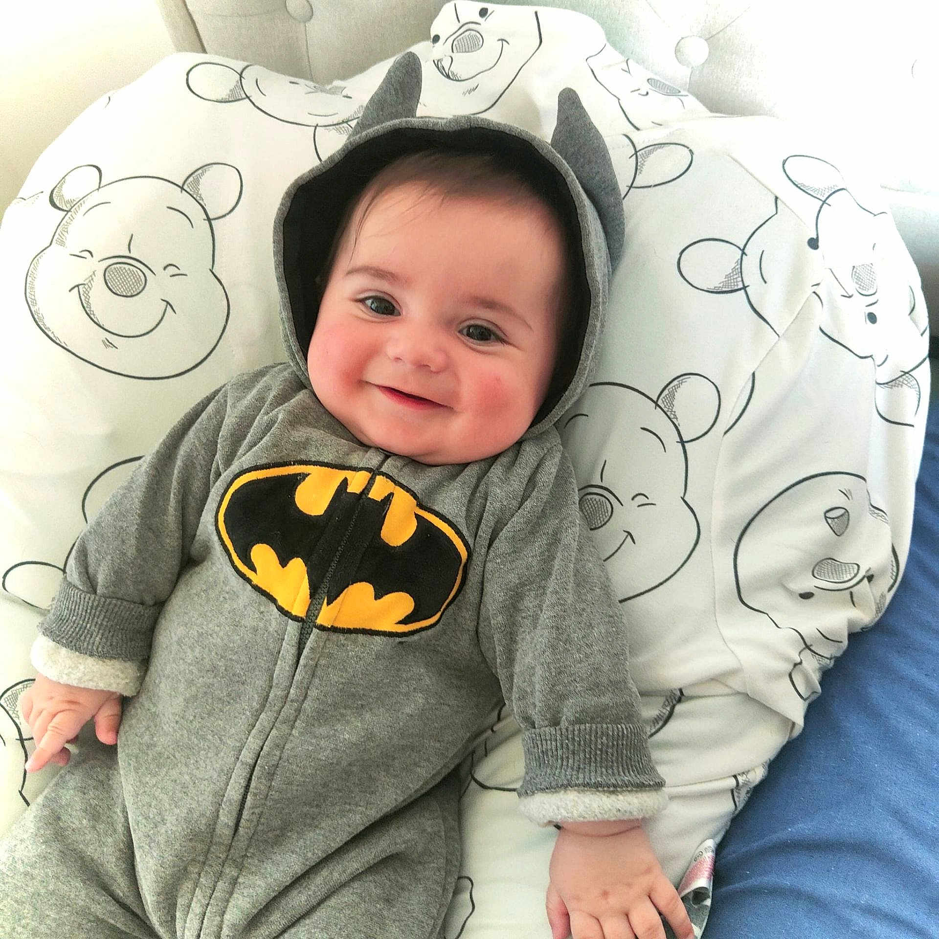 Ange a rejoint le concours — aidez-le/la à gagner de superbes lots ! baby, batman_onesie, child, couch, cute, fabric, face, grey_clothing, hand, happy, hood, indoors, infant, pattern, person, pillow, portrait, smiling, soft, winnie_the_pooh