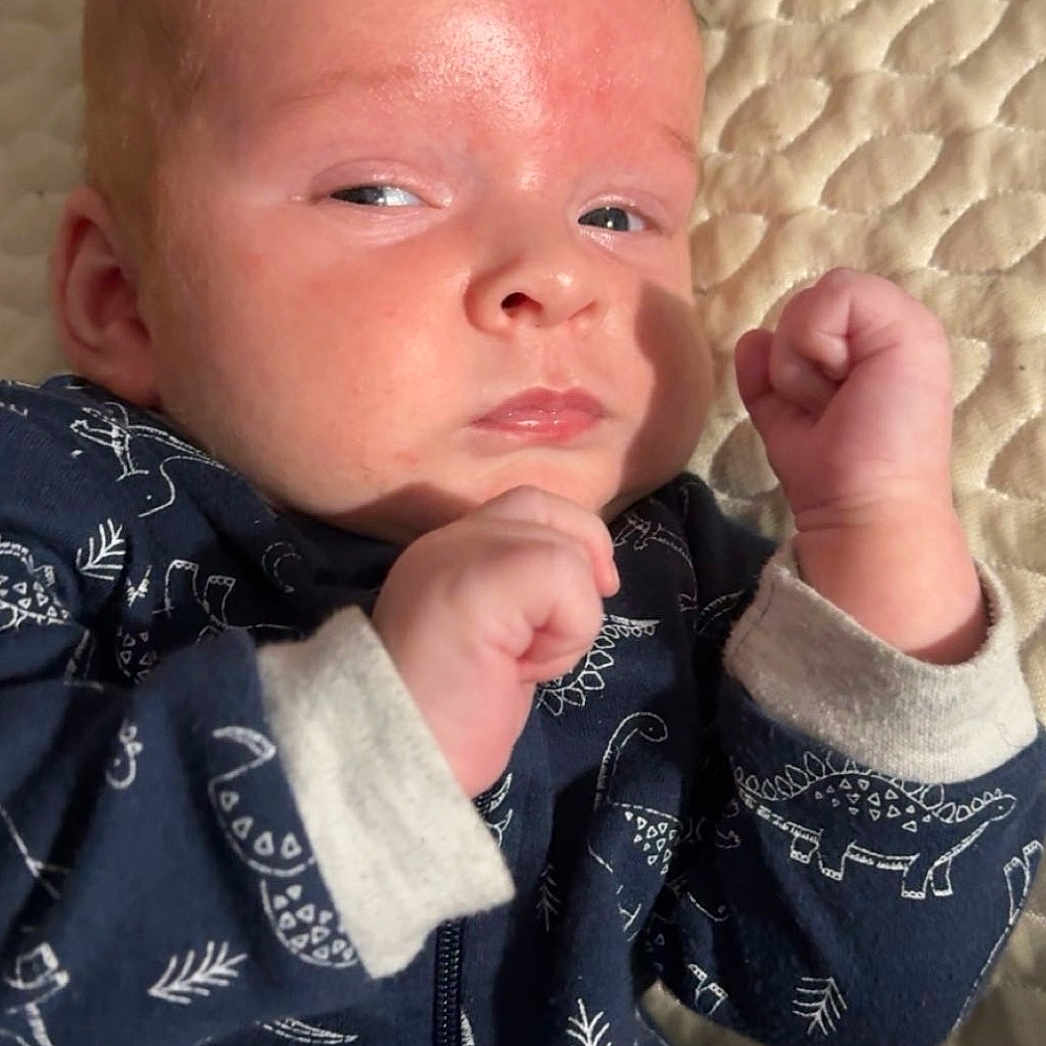 Brock joined the competition — help win amazing prizes! baby, child, closeup, clothing, dinosaur_pattern, expression, face, hair, hand, indoor, infant, mohawk, onesie, person, portrait, pose, quilted_bedspread, skin, sleepwear, young