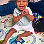 baby, barefoot, child, clapping, colorful, expression, face, floor, frying_pan, happy, household, indoor, person, plastic_bottle, play_mat, polo_shirt, shorts, smiling, toddler, toy