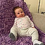 baby, infant, purple_blanket, couch, onesie, socks, knit_texture, indoor, smiling, cute, portrait, child, cozy, relaxed, furniture, home, expression, seated, plush, soft