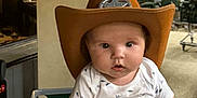 Murdok is registered to the contest to win money with this photo: baby, child, cowboy_hat, sheriff, person, indoor, shopping_cart, deer_head, animal_mount, clothing, curious, holding_hand, face, cute, infant, short_sleeve, white_shirt, blue_shorts, hand, expression