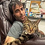 man, cat, tabby_cat, leather_chair, indoor, relaxed, stretching, feline, person, casual_clothing, corkboard, documents, shelf, bottle, insect_spray, medicine, home, whiskers, arm, closeup