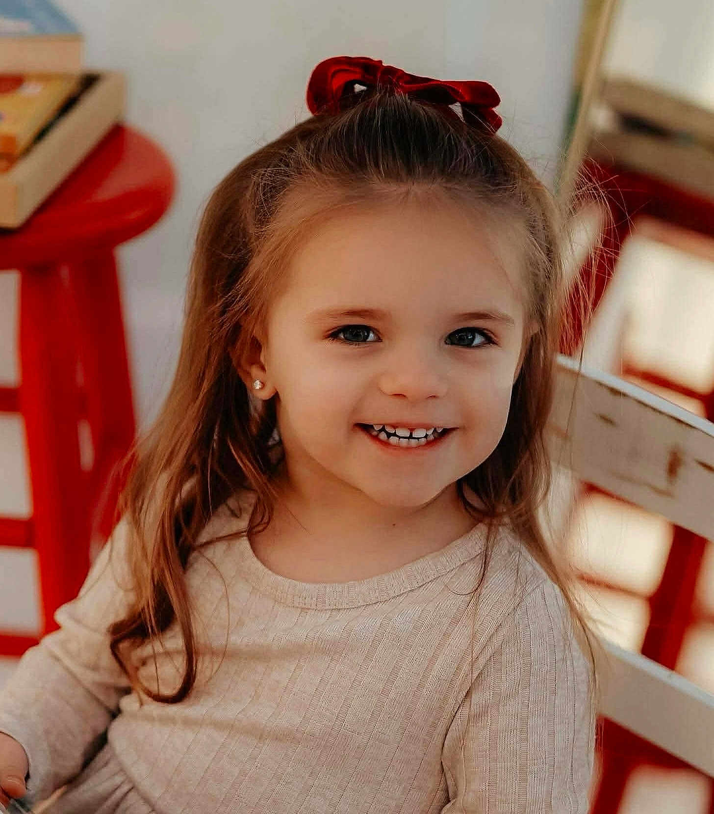 Laney is registered to the contest to win money with this photo: beige_dress, chair, child, cute, earrings, face, girl, happy, indoor, light, long_hair, person, portrait, red_bow, red_stool, sitting, smile, warm, wooden, young