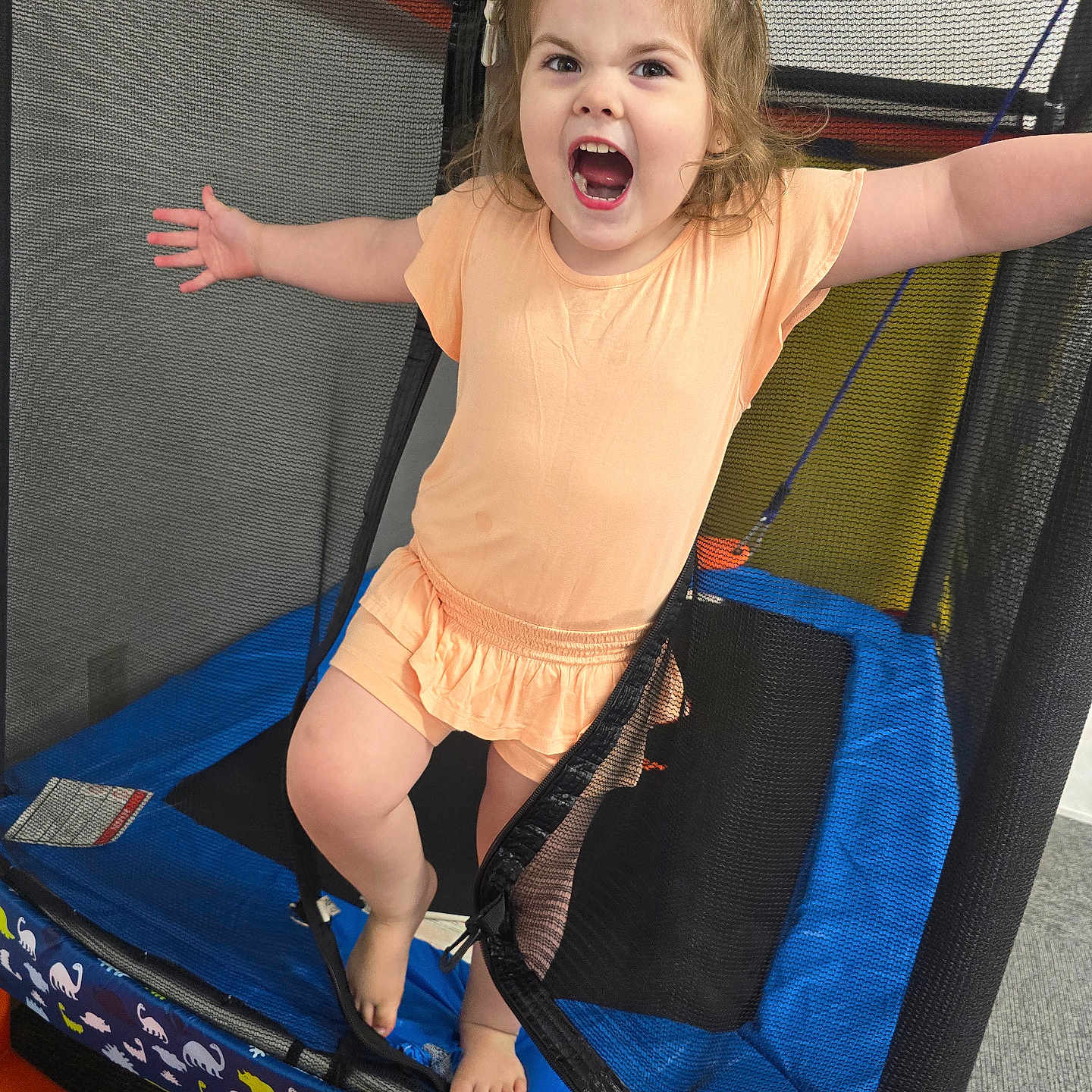 Valeena is registered to the contest to win money with this photo: activity, barefoot, black, blue, carpet, cheerful, child, dinosaur_pattern, expression, fun, hair_buns, indoor, netting, orange, peach_outfit, playful, safety_net, standing, trampoline, young