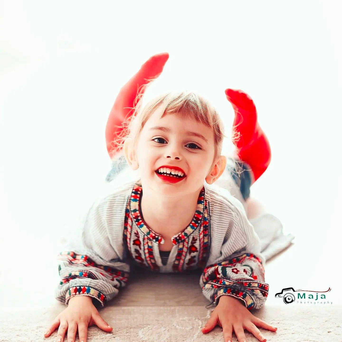 Maja a rejoint le concours — aidez-le/la à gagner de superbes lots ! bright_background, casual_clothing, child, childhood, cute, embroidered_shirt, face, floor, hands, happy, indoor, joyful, light, lying_down, person, playful, portrait, red_socks, smiling, young