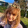 child, girl, flower_crown, outdoor, sunlight, smile, hair, jacket, nature, trees, grass, park, daylight, face, portrait, happy, casual_clothing, young, person, seasonal