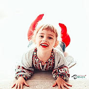 Maja is registered to the contest to win money with this photo: child, smiling, red_socks, patterned_sweater, happy, face, hands, lying_down, carpet, indoor, cute, portrait, young, playful, light_background, bright, joyful, person, feet, casual_clothing