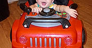 Lucas joined the competition — help win amazing prizes! baby, child, toy_car, walker, smiling, happy, indoor, portrait, face, steering_wheel, red, vehicle, playtime, sitting, bare_feet, wooden_floor, door, home, infant, looking_at_camera