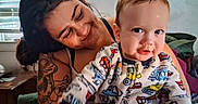 Lucas is registered to the contest to win money with this photo: baby, child, adult, parent, portrait, smiling, sitting, indoors, home, window, blinds, couch, tattoo, holding, infant, face, clothing, colorful, vehicles, family